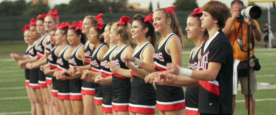The cheerleaders link pinkys during a football game while the school song plays. The cheerleaders spend many hours every day during practice making sure their routines are perfect for competitions.
