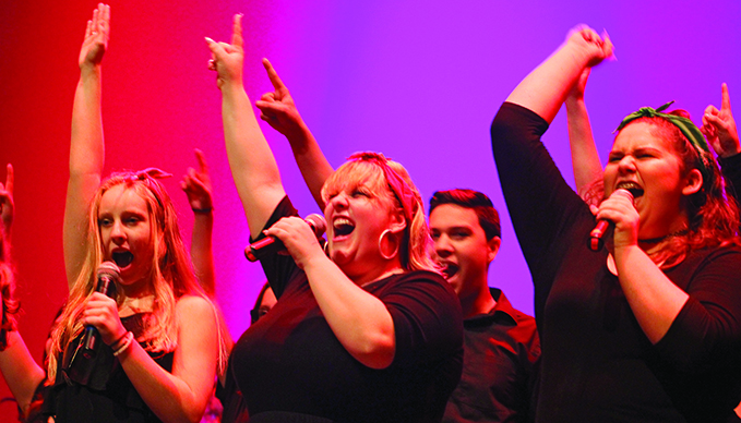 SHOUTING LOUD: Sophomore Lexi Lornez (left), senior Crosby LaGrone (center), sophomore Eric Larson (center right), and sophomore Catalina Hill (right) join their voices for one last shout as the show comes to its close. On the stage, every cast member wears their colored handkerchief proudly as they join in to fill the theater with the ear-vibrating shout. PHOTO BY Preston Rolls