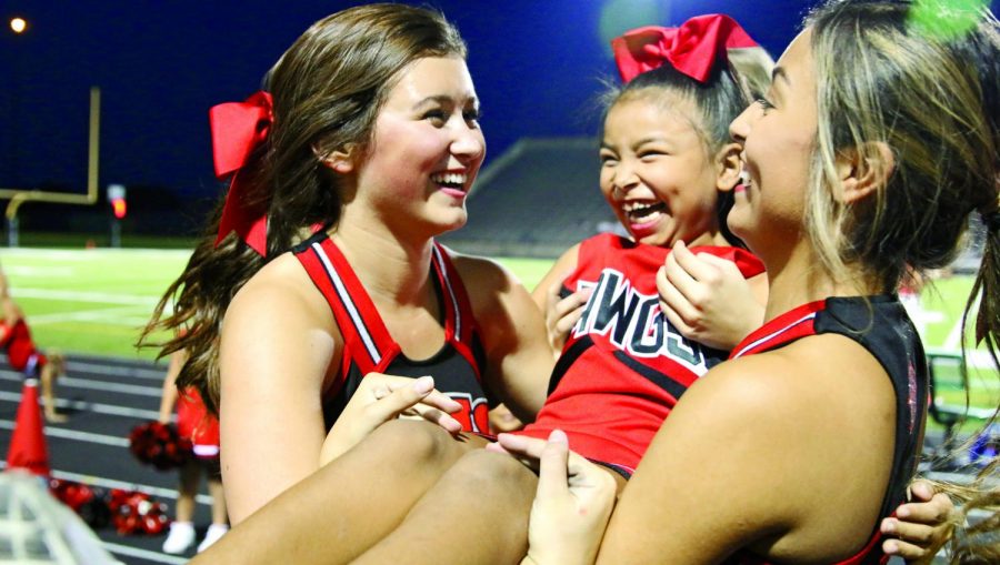 ALL SMILES: Senior varsity captain Jordan Bailey and senior Eliza Lopez cradle a youth cheerleader as she comes down from a stunt. Youth cheer teams preformed with the team at the Bowie v. Vista Ridge game. “Youth teams from around Austin get to come and cheer on the sidelines with us,”Bailey said. PHOTO BY Violet Glenewinkel