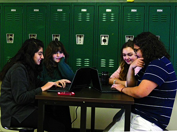 SOCIAL RECHARGE: Juniors Simone Saiyed, Phil Brual, Mia Moore, and senior Sarah Baber do homework at one of the hallway tables. The tables also have the ability to charge various devices.