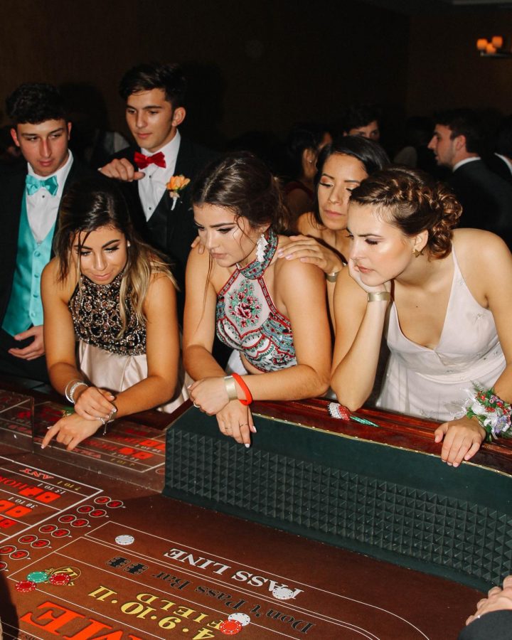 OH CRAP: Gathered around, senior Sophia Ahrens, Madison Horner and Avery Schmidt intensely watch their mock game of Craps. There was a separate room full of mock games such as poker and black jack. ‘’Having all the gambling tables was a fun way to take a break from the dancing, it festivities,” Horner said. 