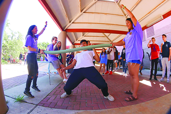 CHEERING ON: Seniors Alexa Robinson and Taylor Bhuiyan cheer on Junior Hector Garcia as he bends back while playing limbo. The Bowie carnival consisted of many different games and activities which the students could participate in. “I thought the carnival was really fun time and a good way to relieve some stress,” Bhuiyan said. “It  brought Bowie students together despite our differences.”