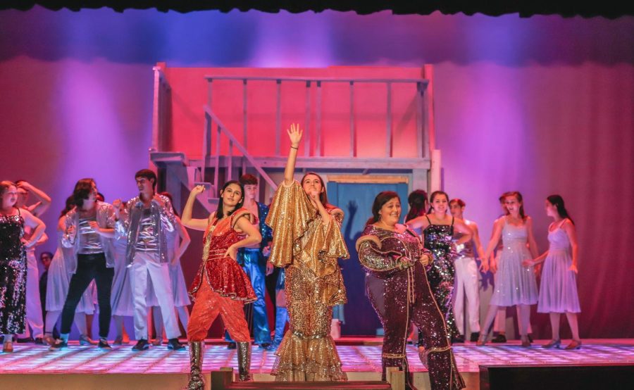 POSED WITH THE DYNAMOS: Seniors Grace Clark, Jamie Forst and Saylor Dement finish off the iconic song "Dancing Queen" as they take a stance at the front of the stage. Some of the main characters, such as Donna, who was played by Jamie Forst, had up to 10 cosQtume changes throughout the show. "We have a dressing room where we keep all our costumes, but we only have one really quick change," Forst said. "We have to put our big sparkly finale costumes on in less than a song and it takes both of my doubles to help me make that costume change."