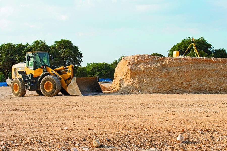 DOWN IN THE DIRT: A front loader is parked by the dirt mound which will be a part of the mound in the parking garage. The laser mounted on the tripod on top of the mound is used to establish grade and elevation of the parking garage.  