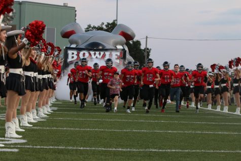 HARD AT WORK: The varsity football tam runs on to the field to begin a game. Photo by Peter Dang