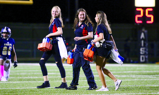 HANDING OUT WATERS: Seniors Cara Spradling, Sarah Clements, and Caitlyn Sanchez walk off the field from delivering water to the players.  Spradling has been a trainer for two years and has seen lots of injuries. “This one kid on the freshman team had bursitis and I got to tape it and when we got back to the trainers got to help pop and drain it,” Spradling said. “I really enjoyed it because I got hands on experience with injuries.” 