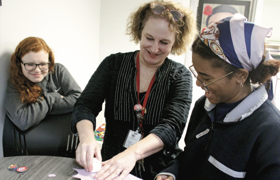 VALENTINES CREATIONS: Librarian Tara Walker-Leon demonstrates how to use a heart shaped hole puncher to juniors Megan Shaver (left) and Amara Robertson (right). In order to promote creativity and art production, Walk- er-Leon hosts the MakerSpace every Monday and Friday during FIT.