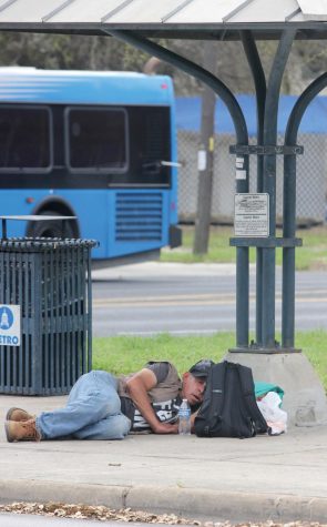 WAITING FOR THE BUS: A man sleeps on the ground at a bus stop with his belongings beside him. Bus passes along with bottle water are some of the most commonly needed resources among homeless people. “People need to get places and it’s hard when you don’t have money for lunch or transportation,” Sunrise Church volunteer coordinator Sarah Combs said. “So then rather than giving them money I give them a bus pass, and then I personally also have business cards for Sunrise so that they know we have resources available to them if they want to use them.”