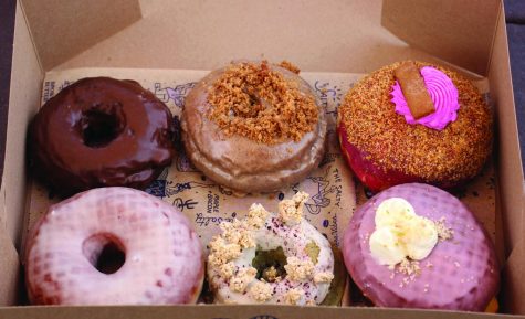 Freshly Baked: The Texas Chocolate Sheet cake, Coffee Cake, Dragon and Passion Fruit, Classic Glazed, Gluten-Free Blueberry Pancake, and Prickly Pear Margarita donuts sit in their box before being devoured. The Salty Donut offers seasonal rotating flavors and year-round flavors.