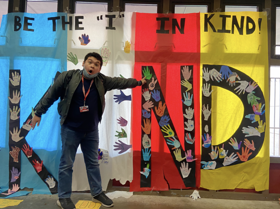 BEING+THE+I+IN+KIND%3A+sophomore+Brett+Rice+poses+in+front+of+the+kindness+poster+outside+of+A+hall.+The+poster+features+hand-shaped+cutouts+with+encouraging+messages+on+them.+