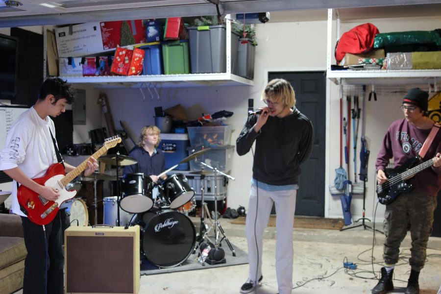 JAMMING OUT: Seniors Caiden Kinsey (far left), Mac Allen (left), Ace Brown (right), and John Michael Rocha (far right)practice one of their original songs in their garage. You can stream Track Five’s songs on Spotify. 