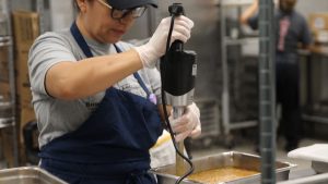 A cafeteria worker is mixing beans, preparing for the student lunch rush. These beans will be served to the students on trays with other foods.