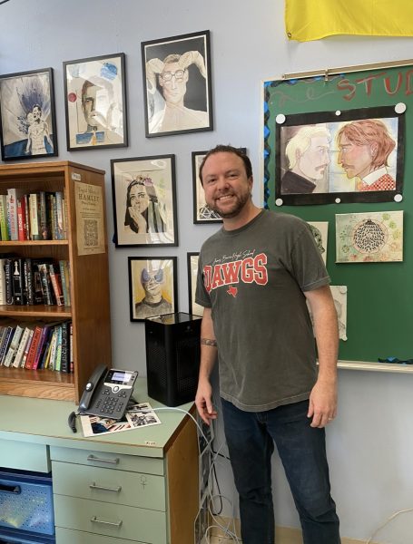 POSING WITH THE MASTERPIECES: Flick stands proudly in front of his art work. Hung on the back wall of his classroom, all students are welcome to admire his work and add their own contributions. 