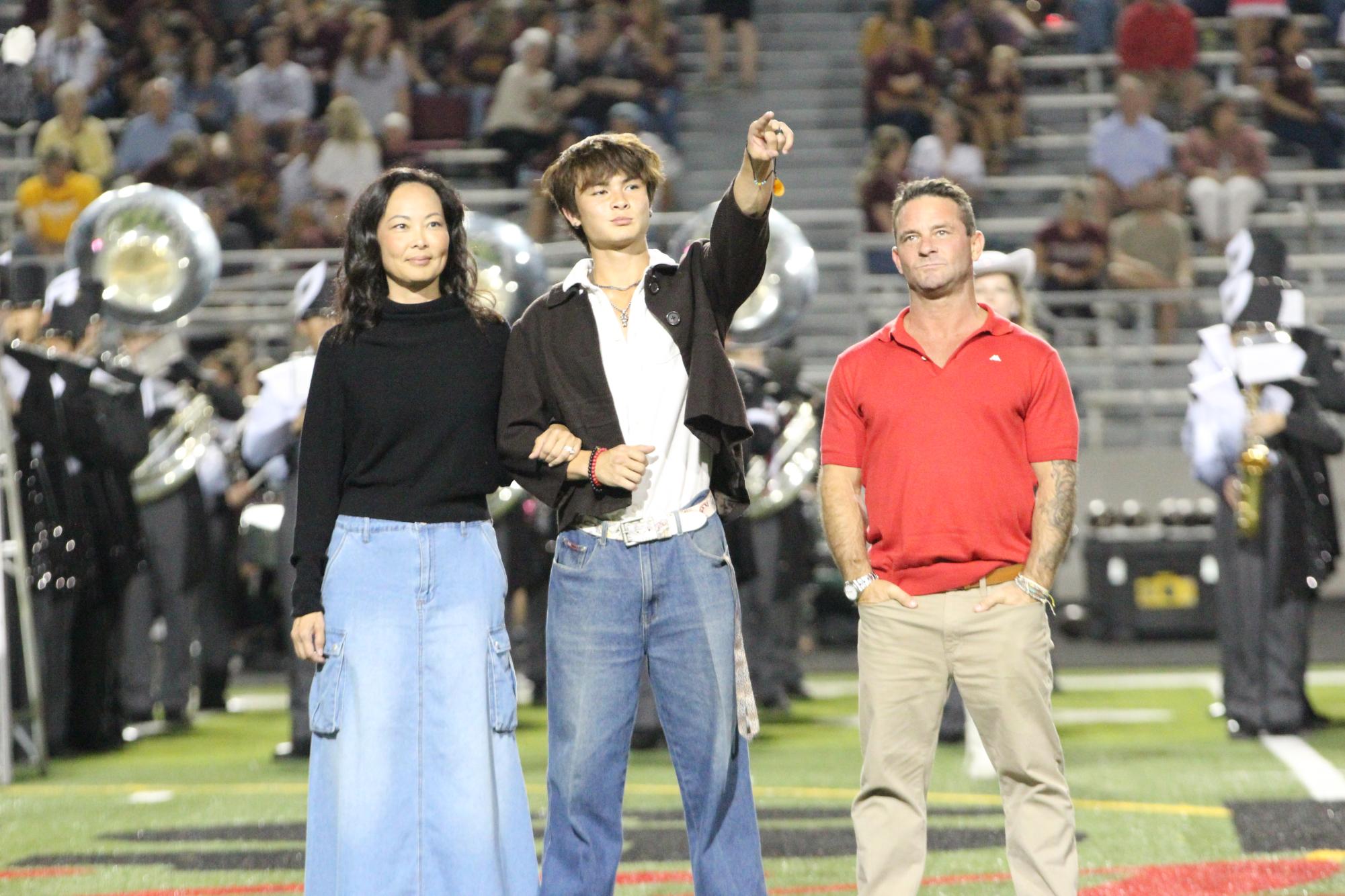 POINTING TO THE CROWD: Senior Caden Delk points to his friends as he is escorted on the field by his parents. Delk thanks his good friends, family, and favorite music artists for his nomination.  “My favorite part was getting to fill out the homecoming court sheet and hearing them announce my plans to become the king of Fiji,” Delk said