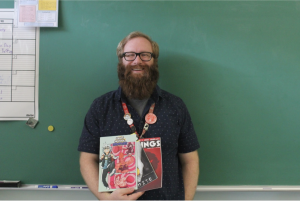 AP English Language and advanced English 1 teacher poses in his classroom with some of the comic books he's helped create over the years. 