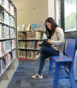 TRYING IT OUT: Junior Serra Gomez skims a book she grabbed off the shelf while sitting on the MLK memorial bench in the Austin public library. Gomez does this before deciding to check out the book online.