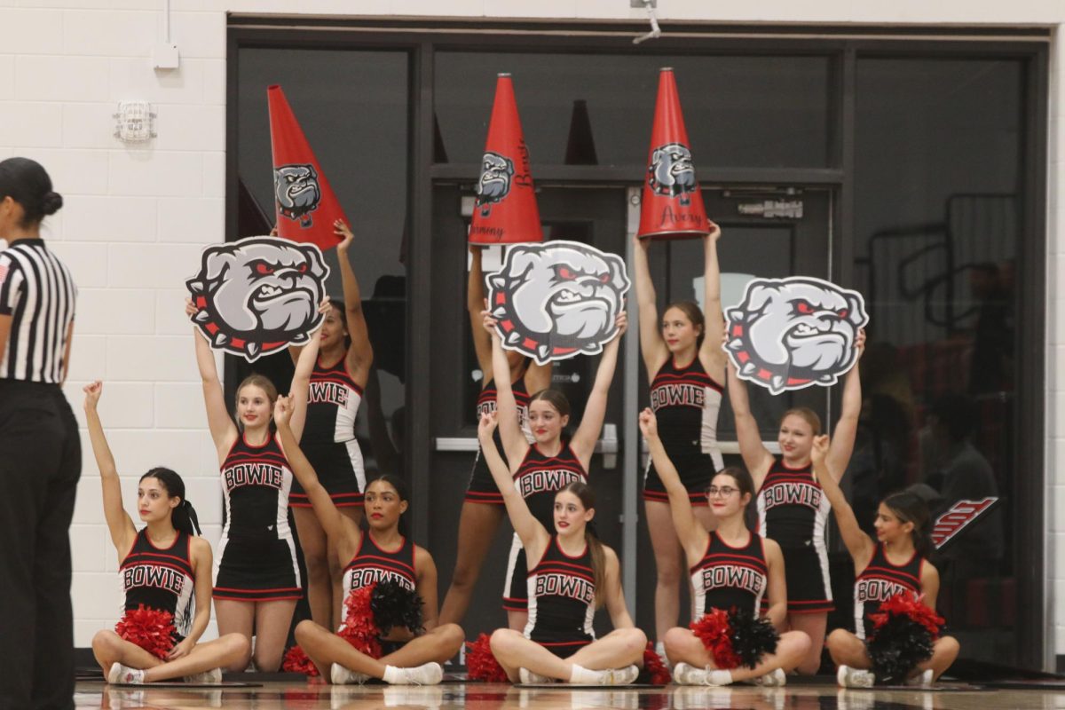 TEAM SPIRIT: Sitting on the sideline, Bowie’s cheer team shows support during a basketball game. This year cheer decided to combine JV and varsity teams to help maximize support for Bowie’s sports teams.